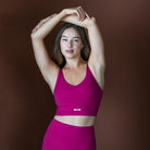Woman wearing a pink sports bra and leggings with a brand logo on a brown background