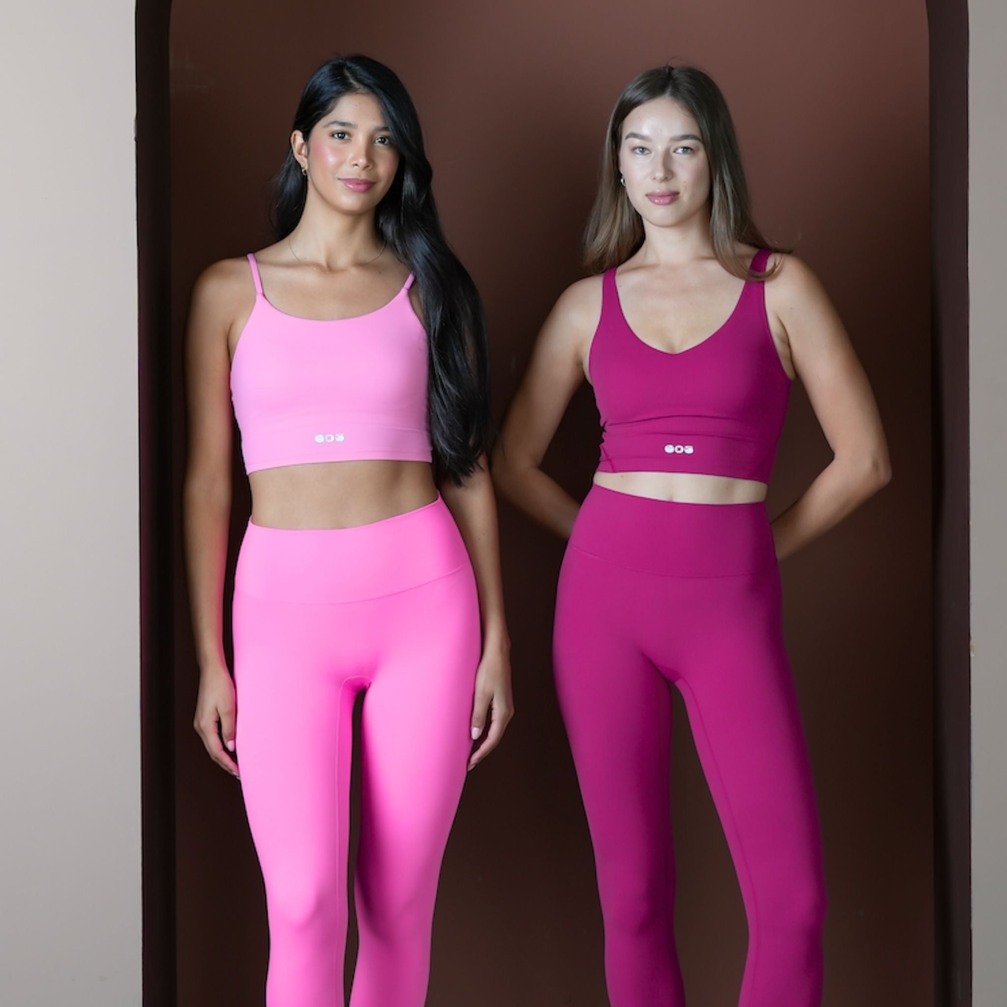 Two women wearing pink athletic outfits against a brown background