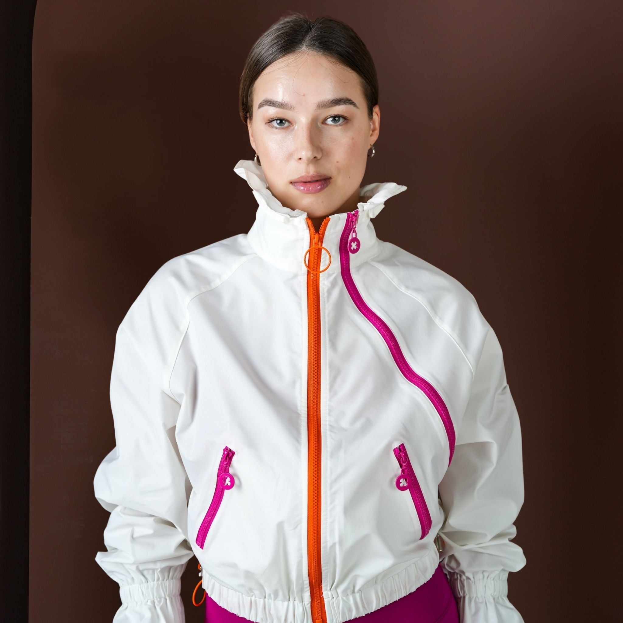 Person wearing a white jacket with pink accents on a brown background