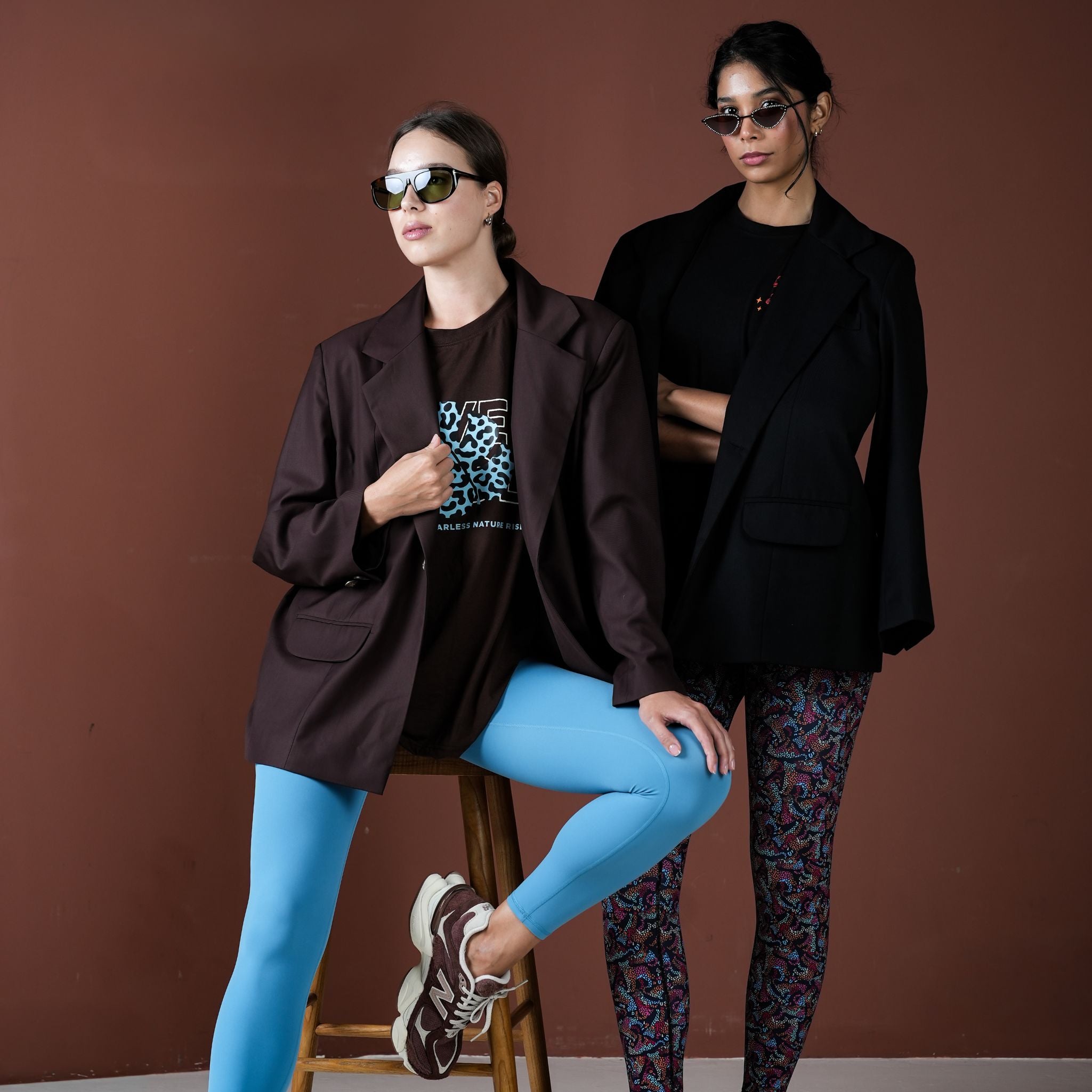 Two women posing against a brown background wearing stylish outfits with jackets and leggings.
