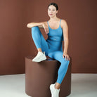 Woman in blue athletic wear sitting on a brown cylindrical block against a brown background