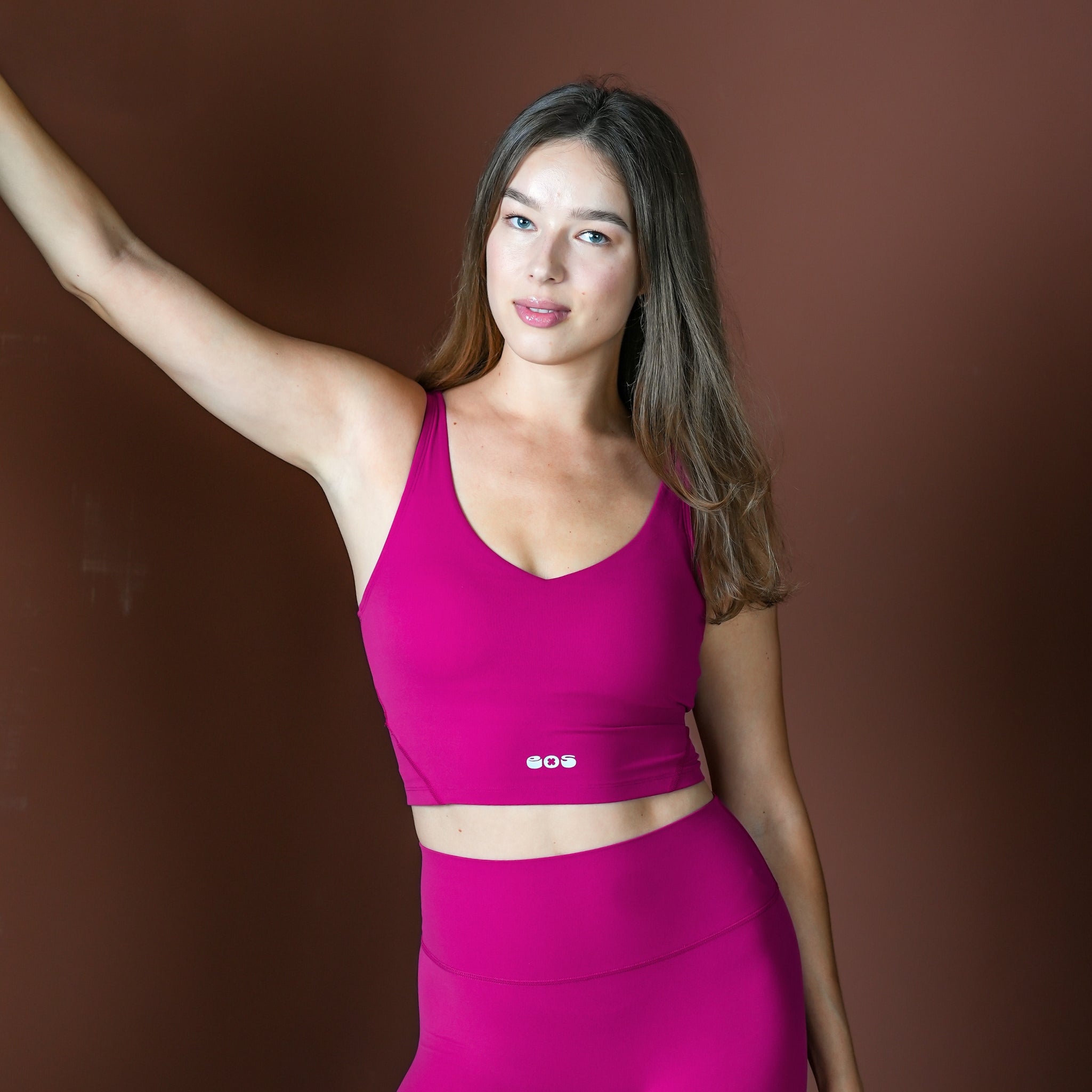 Woman wearing a pink sports bra and leggings against a brown background